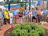 A group of adults stands outdoors on a brick patio with an American flag and two dogs in front.