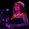 Singer onstage beside a microphone under purple lighting.