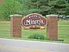Brick entrance sign reading Welcome to Minerva Est. 1833 beside a road.