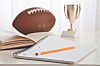 Football marked MVP beside an open notebook, pencil, and trophy on a desk.