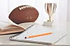 Football marked MVP beside an open notebook, pencil, and trophy on a desk.