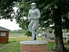 Stone statue of a football player on a brick pedestal in a park near trees and buildings.