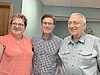 Three people standing together indoors, smiling at the camera.