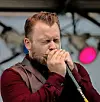 A male singer closes his eyes while singing into a handheld microphone on stage.