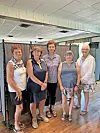 Five women posing together in a hall with racks of clothes behind them.