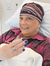 Smiling woman in a hospital bed holds up her hand with blue nail polish.