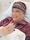 Smiling woman in a hospital bed holds up her hand with blue nail polish.