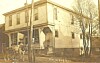 Sepia-toned image of a two-story house with a porch, trees, and a bicycle in front.