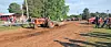 Orange tractor grading a dirt track with people watching from the sides.