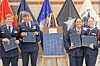 Four cadets in uniform holding awards stand beside a display board with flags in the background.