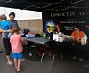 People standing by an outdoor booth under a black canopy with tables and supplies.