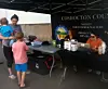 People standing by an outdoor booth under a black canopy with tables and supplies.