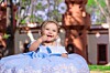 Smiling child in a light blue dress sitting outdoors in front of a building.