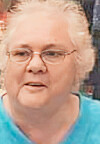 Close-up of a woman wearing glasses and a light blue top.