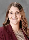 Studio portrait of a smiling woman in a burgundy blazer against a gray background.