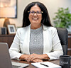 Woman smiling at a desk with a laptop, notebook, and mug in an office.
