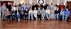 Large group posing for a portrait in a formal room with chandeliers and a polished wooden floor.