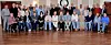 Large group posing for a portrait in a formal room with chandeliers and a polished wooden floor.