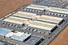 Aerial view of a large industrial complex with several long buildings and parking areas.