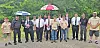 Group of people standing on a dirt road with umbrellas in a green outdoor setting.