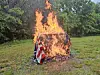 A blaze engulfs a small object wrapped with an American flag in a grassy field.