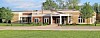 Exterior of a low-rise school building with brick and beige siding, a covered entrance, lawn, and road.