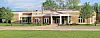 Exterior of a low-rise school building with brick and beige siding, a covered entrance, lawn, and road.