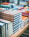 Stacks of cookbooks arranged on a table with colorful books in the background.