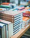 Stacks of cookbooks arranged on a table with colorful books in the background.