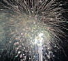 Fogos de artifício dourados e brancos explodem no céu noturno escuro.