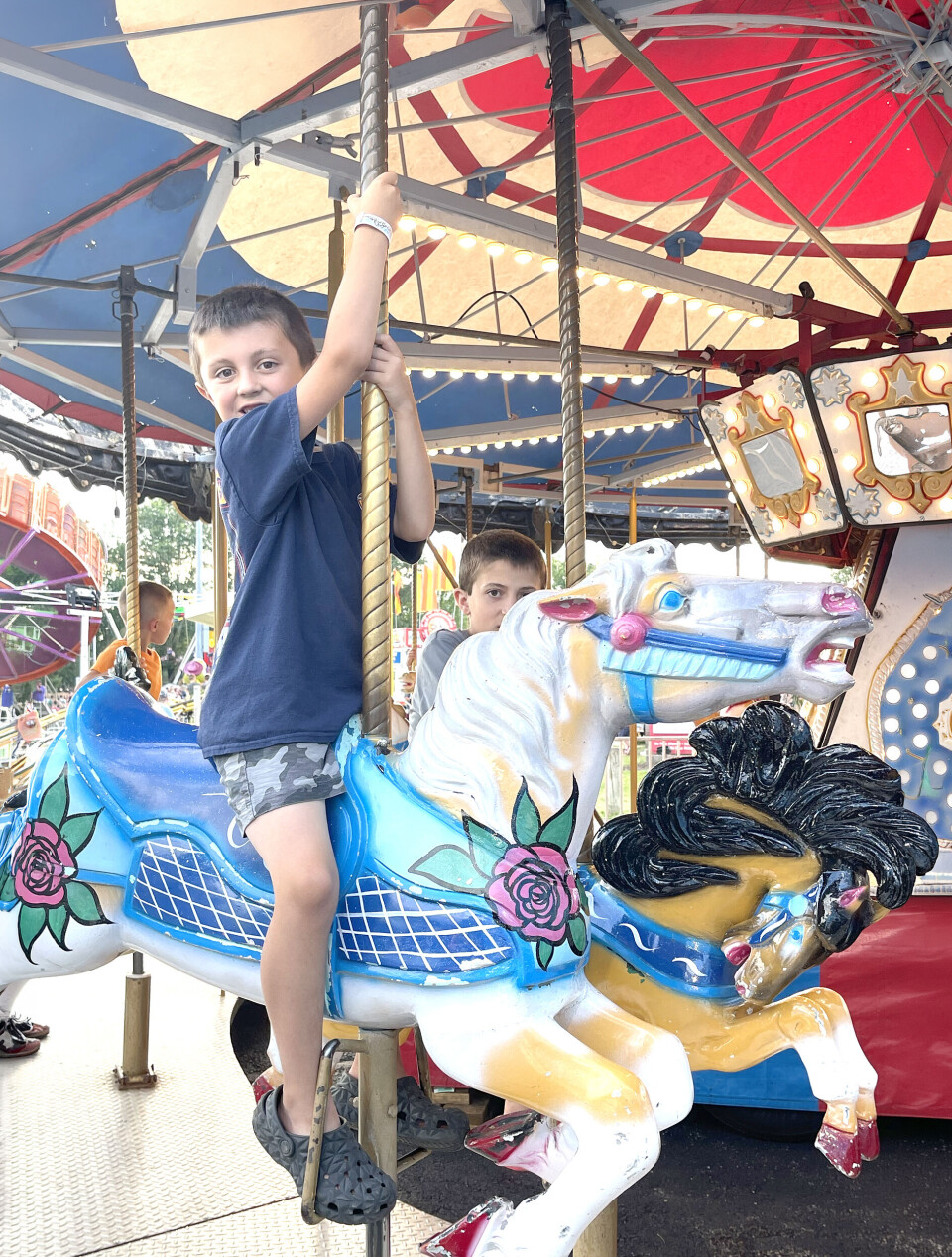 Dos niños sobre un caballo de carrusel azul y blanco bajo un dosel rojo y azul.