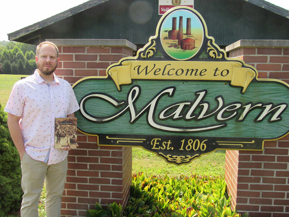 CCM/Thomas ClapperJason Lombardi is shown holding his new book, “Images of America Around Malvern,” at the corporation sign to the village where he grew up. The book, a pictoral history of the village, is available online at major retailers and at Books-A-Million at The Strip in Canton.