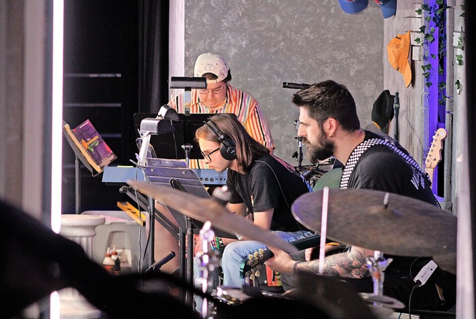 Musicians rehearsing on stage with drums, guitars, microphones and music stands.