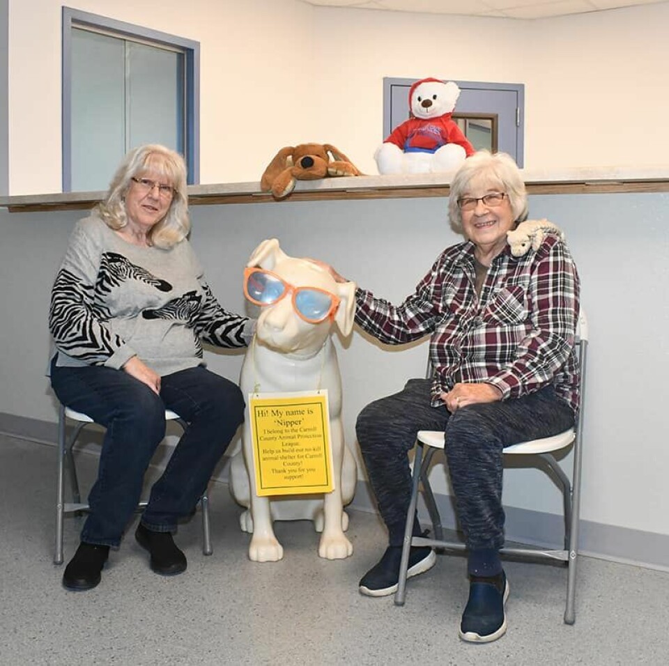 CCM/ Carol McIntireCarroll County Animal Protection League Vice President Lorna Lowell-Whaley (left) and President Eileen Rohrer take a break from preparing for a Nov. 12 open house. The officers are sitting with Nipper, the group’s mascot, who will greet visitors in the lobby.