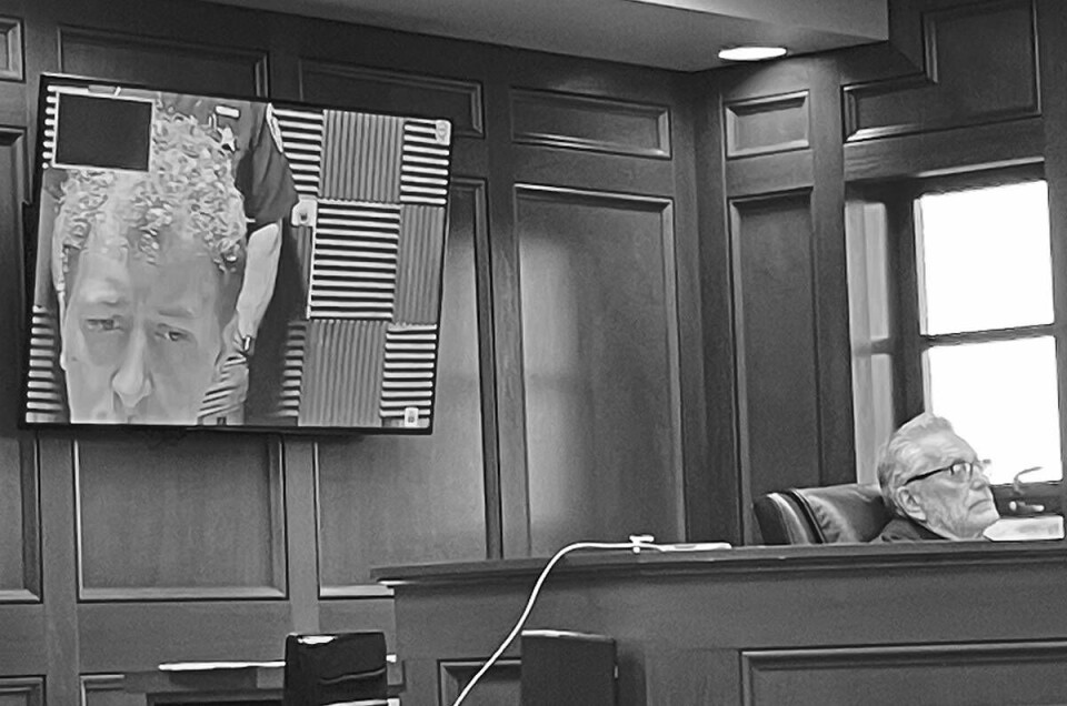 Carroll County Municipal Court Judge Gary Willen (right) watches a video screen on the bench via which Michael L. Geclker appeared for a hearing weeks ago. Geckler can be seen on the larger screen at left.