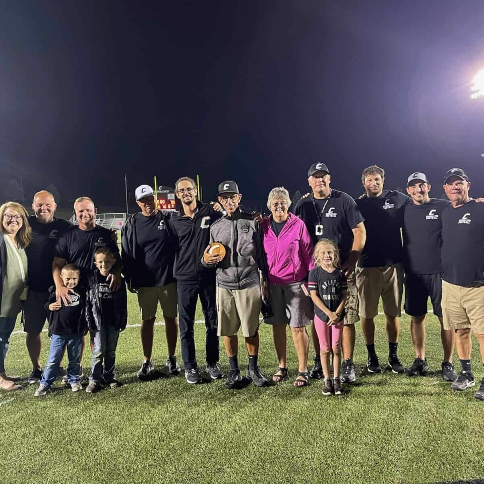 Carrollton Coach Jim Tsilimos (holding football) is surrounded by his coaching staff, family and friends after winning his 200th career game Friday evening.