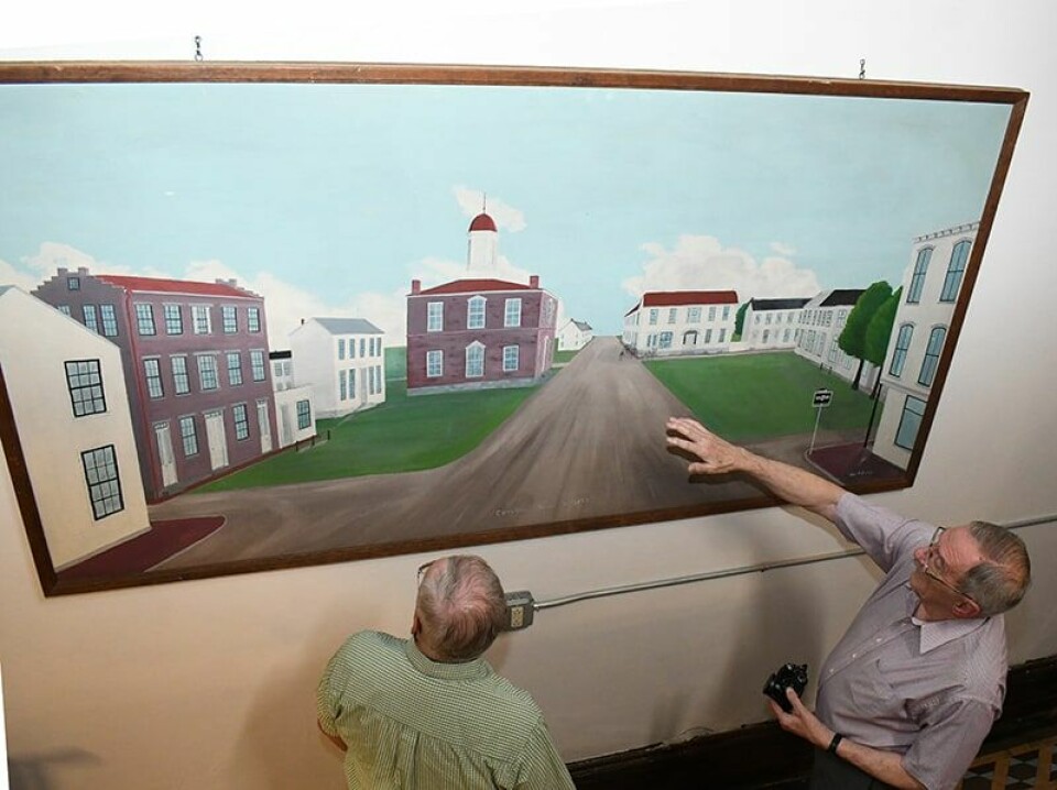 CCM/Carol McIntire Carroll County Commissioner Bob Wirkner (left) and Don Butler discuss the historic Carrollton painting created by Butler’s father, Joe, in the late 1950s. Joe Butler died before the painting was finished. The painting is now in the studio of his grandson, Curtis Butler, where it will be finished and returned to Carrollton. The painting hangs on a second-floor wall in the county courthouse.