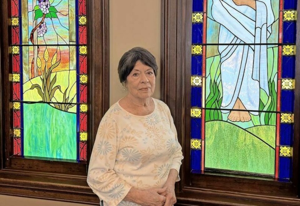 Pat Thompson, member of Fredericksburg Presbyterian Church, poses with two stained-glass windows she designed. Thompson and 11 other members dedicated 16 years to designing, constructing and installing 12 windows to beautify their church. Fredericksburg Presbyterian windows project completed