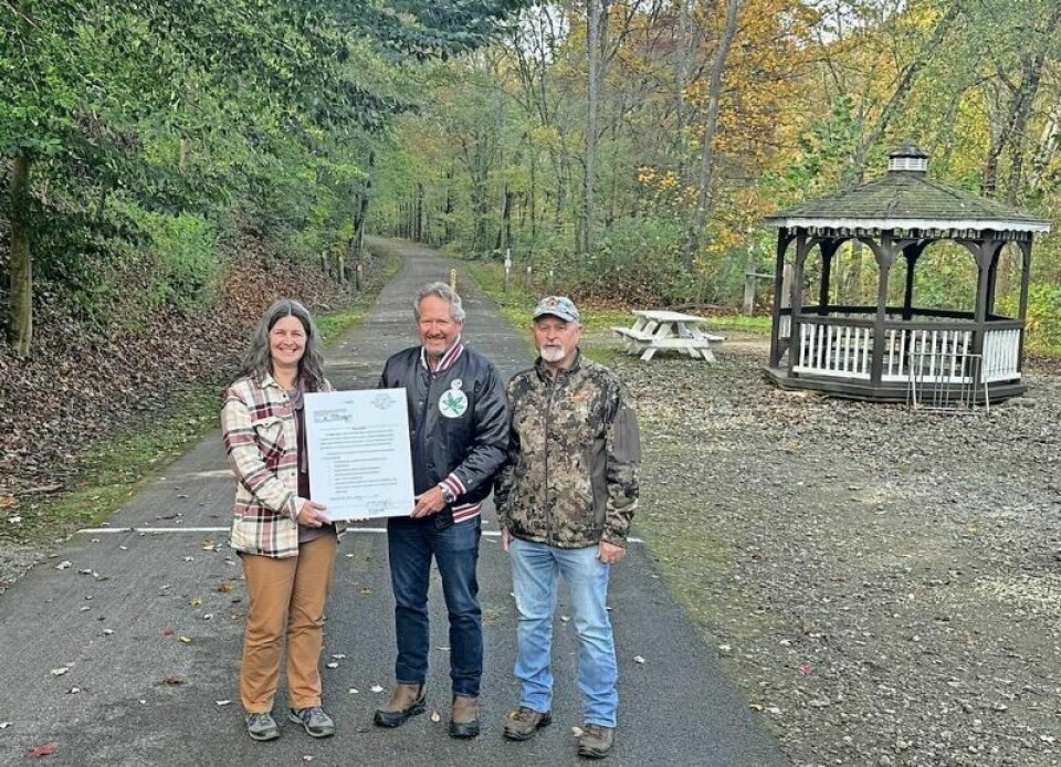 Holmes County Park District Director Jen Halverson, left, and board member Dan Mathie flank Bill Baker in a presentation of a copy of the deed that gave the Holmes County Rails to Trails Coalition more control over the trail area near Glenmont. Baker donates Glenmont land to park district