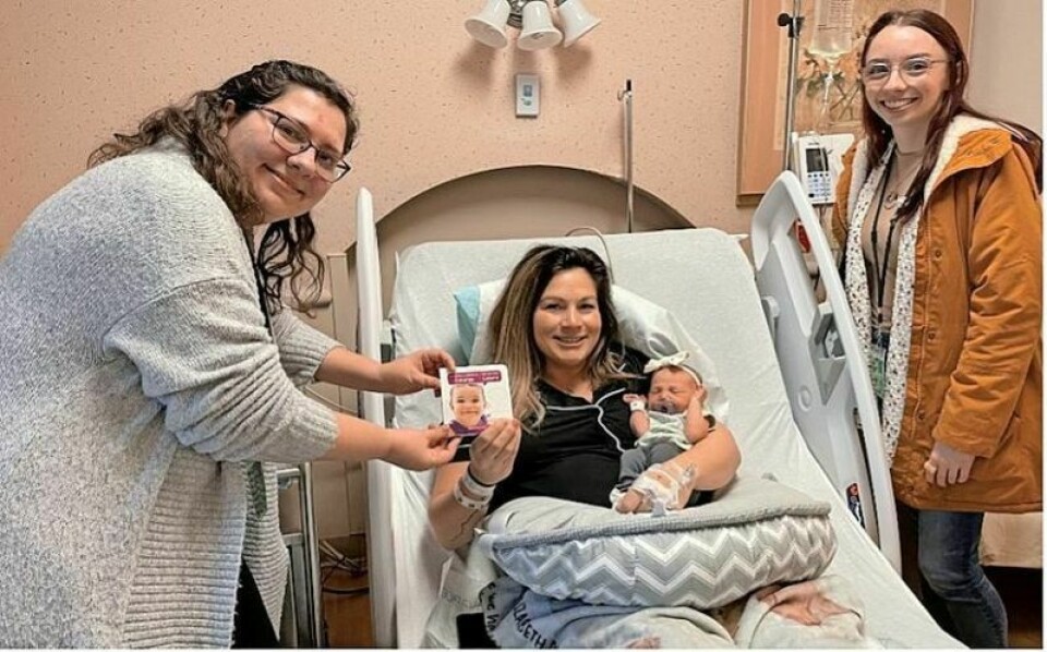 TCPL children’s services manager Mary Smrek and public relations associate Marisa Bleininger hand a book to Staci Dunn and her newborn daughter Dylan at Cleveland Clinic - Union Hospital. Trust provides books for all Tusc County babies