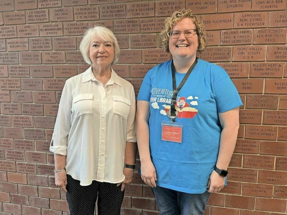 Marsha Fortune, left, head librarian when the new building opened in 1999 with Courtney Wallace, current branch manager. Behind them is the Friends of the Library wall containing bricks that were sold to help fund the project. Library will celebrate 25 years at current location June 13
