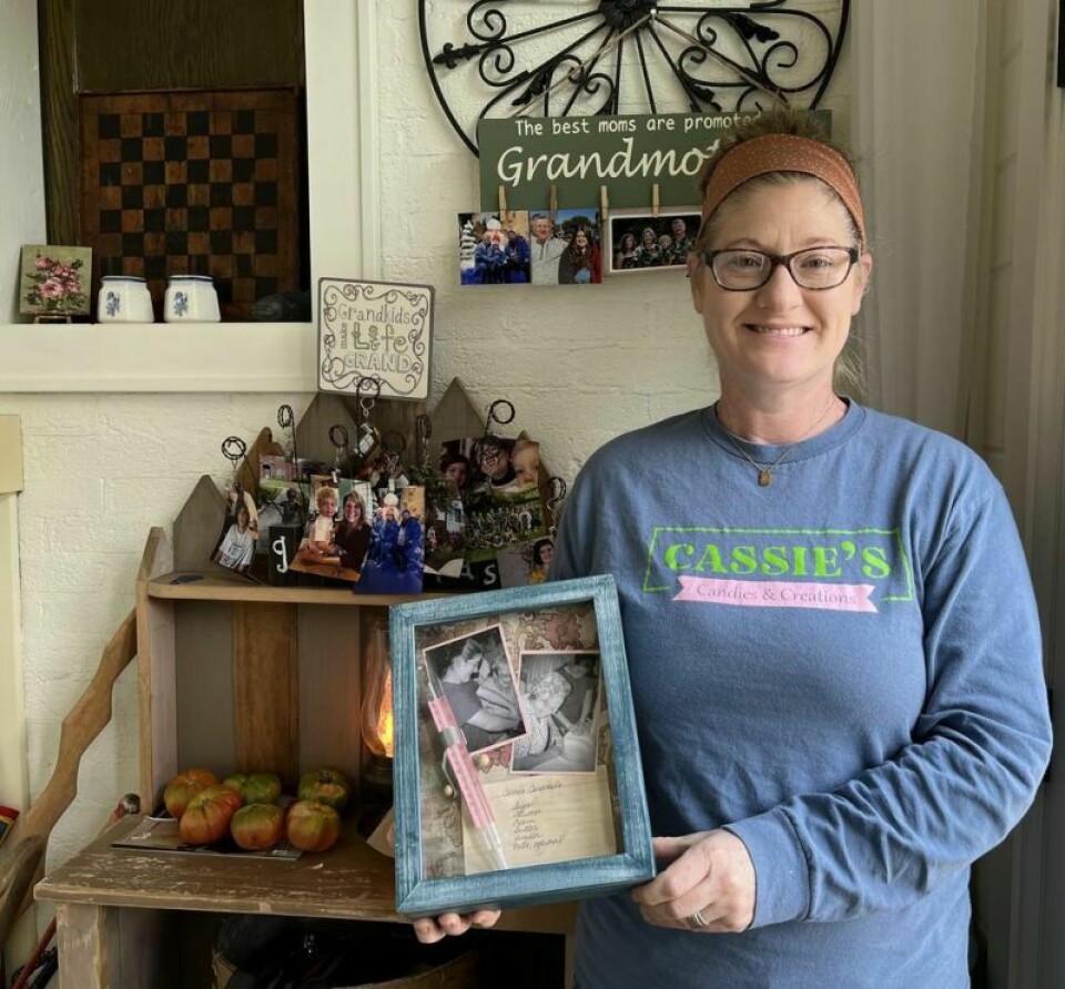 Kara Wolfe, owner of Cassie's Candies and Creations, holds a shadow box displaying photos of Wolfe learning how to bake pies with her great-grandmother Cassie Mase, along with Mase's original caramel recipe and candy thermometer. Family tradition is a recipe for sweet success