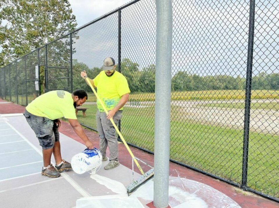 Leo Grizzard, left, and Chandler McGrath from VASCO Asphalt add a layer of glue atop a fiberglass grid, which will be followed by acrylic resurfacer. Basketball courts in park getting new surfaces