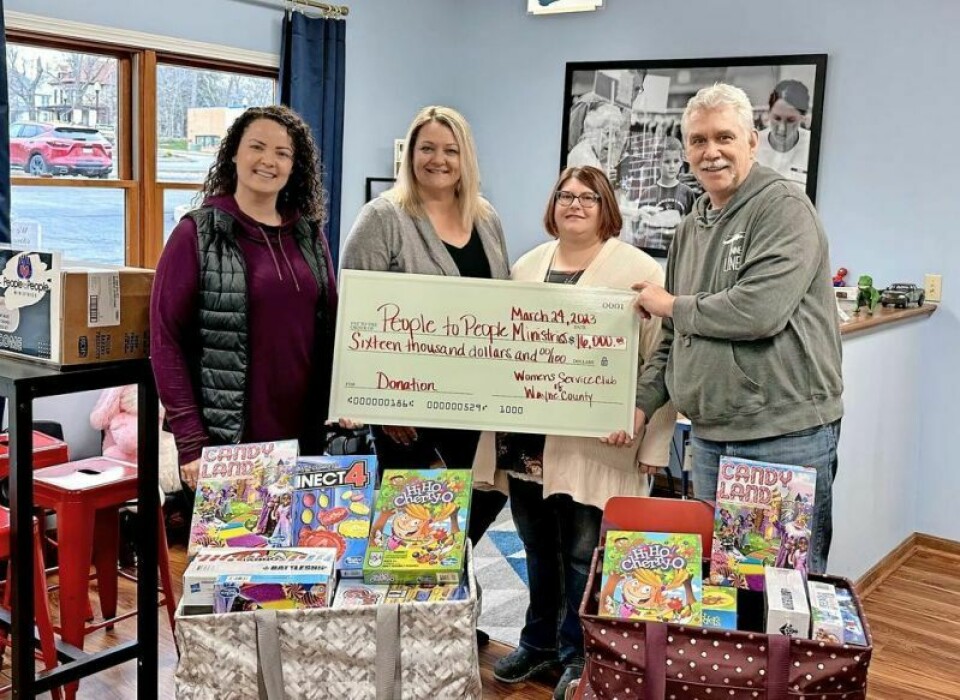 Women’s Service Club members Jenna Poindexter, left, Janell Cooper and Amanda Hill presented a check for $16,000 to People to People Director Joe Szeker, right, after last year’s fundraiser. In front are classic board games the club donated for People to People’s Christmas Project. Hippies and cowboys theme of Feb. 24 P2P fundraiser